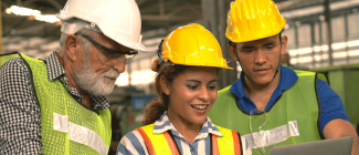 three persons wearing hard hats looking at a clipboard