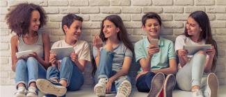 Five pre to early teenagers interacting while sitting against a white brick wall